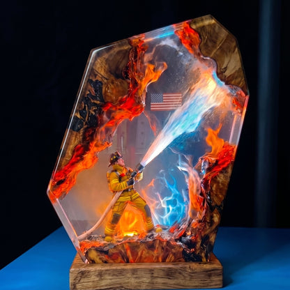 A resin art piece depicting a firefighter in yellow gear spraying water, with vivid orange flames and blue water effects inside a clear, shield-shaped slab mounted on a wooden base.